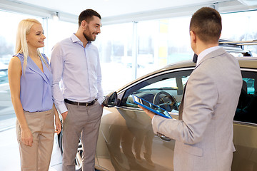 Image showing happy couple with car dealer in auto show or salon