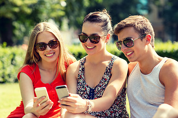 Image showing smiling friends with smartphones sitting in park