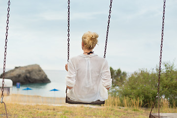 Image showing Young blonde woman sitting on the swing