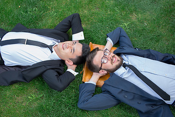 Image showing The two happy young businessmen in a suit lying on the green grass