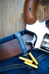 Image showing silvery revolver nagant with cartridges on old blue jeans