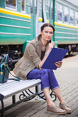 Image showing beautiful middle-aged woman-traveler sitting on a bench, holding