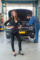 Image showing Sales woman standing in front of a car, being serviced for deliv