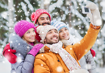 Image showing smiling friends with camera in winter forest