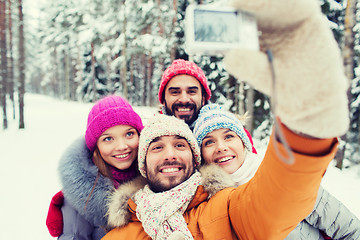 Image showing smiling friends with camera in winter forest