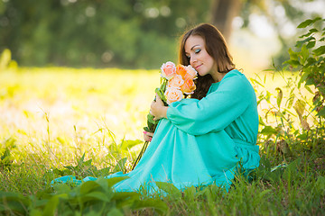 Image showing Young girl smelling a bouquet of roses fragrance under the shadow of the trees in the sunny weather