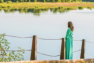 Image showing A young girl stands on the bridge over the river and looks into the distance