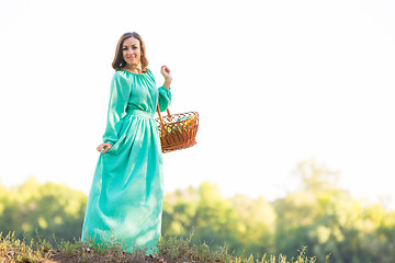 Image showing The girl with a basket in a long dress standing on the hill