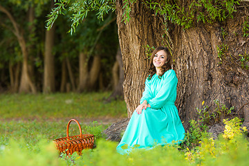 Image showing A girl in a long dress sat by a tree in the woods