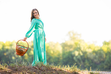 Image showing The girl with a basket in a long dress and in a good mood is on the hill