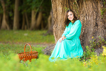 Image showing A girl in a long dress sat by a tree, next to put the cart