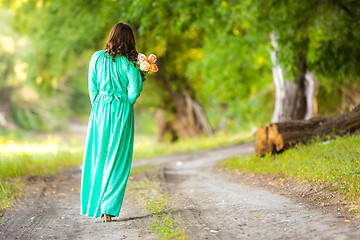 Image showing A girl in a long dress walking along the road with a basket in the hands of