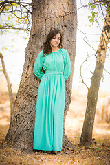 Image showing A girl in a long dress standing near a tree in the woods