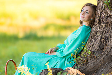 Image showing A girl in a long dress and sat resting at a big tree in the forest