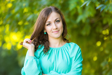 Image showing The waist of a beautiful girl in a dress on a background of blurred green foliage