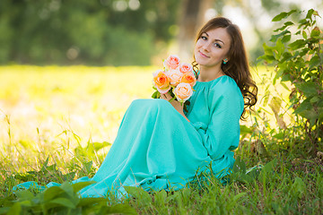 Image showing A young girl sits with a bouquet of flowers under the shade of trees on a sunny day