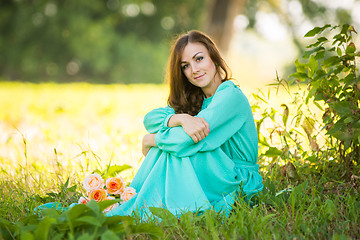 Image showing A beautiful girl sitting under the shade of trees, lies at the feet of her a bouquet of roses