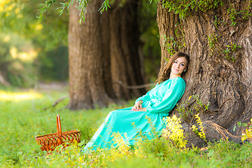 Image showing A girl in a long dress and sat resting at a big tree in the forest