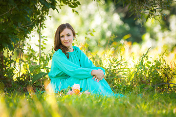 Image showing A girl in a long dress sitting on the grass in the forest in sunny weather