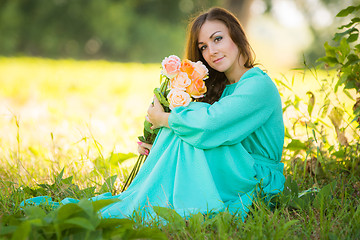 Image showing Portrait of a young girl with a bouquet of roses sitting in the shade of the trees on a sunny day