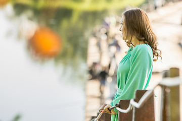 Image showing Beautiful girl stopped on the bridge over the river and looked into the distance