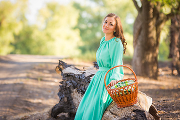 Image showing The girl with a basket in a long dress sat down to rest on an old fallen tree