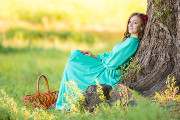 Image showing A girl in a long dress sat down at the old tree in the forest