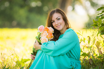 Image showing Portrait of a young girl with a bouquet of roses sitting in the shade of the trees on a sunny day