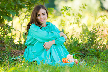 Image showing A girl in a long dress sitting in the shade of the trees on a sunny day