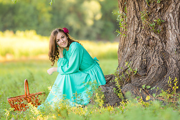 Image showing A girl in a long dress in a good mood crouched near a tree in the woods