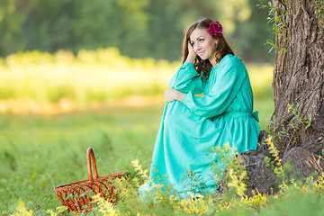 Image showing A girl in a long dress and sat down at the thought of an old tree in the forest