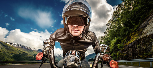 Image showing Biker in helmet and leather jacket racing on mountain serpentine