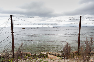 Image showing barb wire fence over gray sky and sea