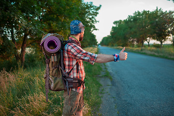 Image showing Young caucasian tourist hitchhiking along a road.