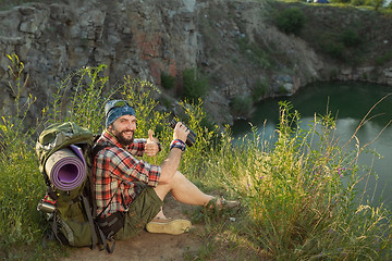 Image showing Young caucasian man with backpack sitting on the top of hill