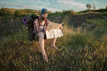 Image showing Young caucasian man with backpack sitting on the top of hill