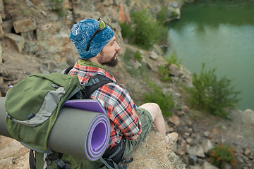 Image showing Young caucasian man with backpack sitting on the top of hill