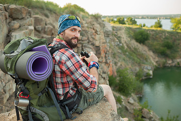 Image showing Young caucasian man with backpack sitting on the top of hill