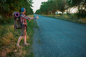 Image showing Young caucasian tourist hitchhiking along a road.