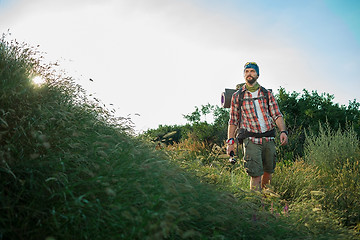 Image showing Young caucasian man with backpack walking on a green meadow