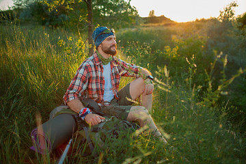 Image showing Young caucasian man with backpack sitting on the top of hill