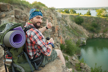 Image showing Young caucasian man with backpack sitting on the top of hill