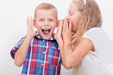 Image showing Teenage girl whispering in the ear of a secret teen boys on white  background