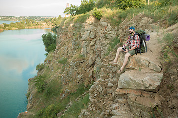 Image showing Young caucasian man with backpack sitting on the top of hill