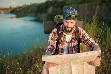 Image showing Young caucasian man with backpack sitting on the top of hill