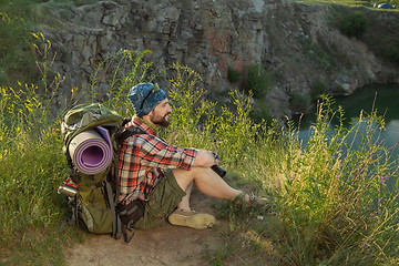 Image showing Young caucasian man with backpack sitting on the top of hill