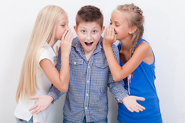 Image showing Teenage girsl whispering in the ears of a secret teen boy on white  background