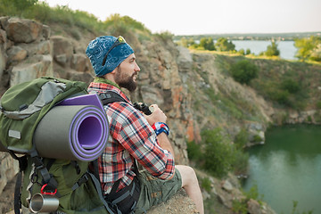 Image showing Young caucasian man with backpack sitting on the top of hill