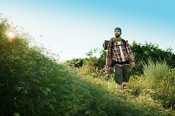 Image showing Young caucasian man with backpack walking on a green meadow