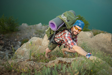 Image showing Young caucasian man with backpack rising on the rock